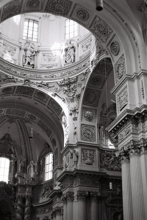 The interior of a church features ornate arches, columns, and statues, with light streaming through windows in the dome.