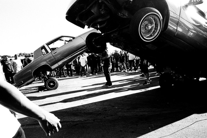 Two lowrider cars are bouncing on their hydraulic suspensions in front of a crowd of people.