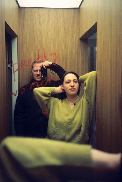 A man and a woman are reflected in a mirror with red writing on it.