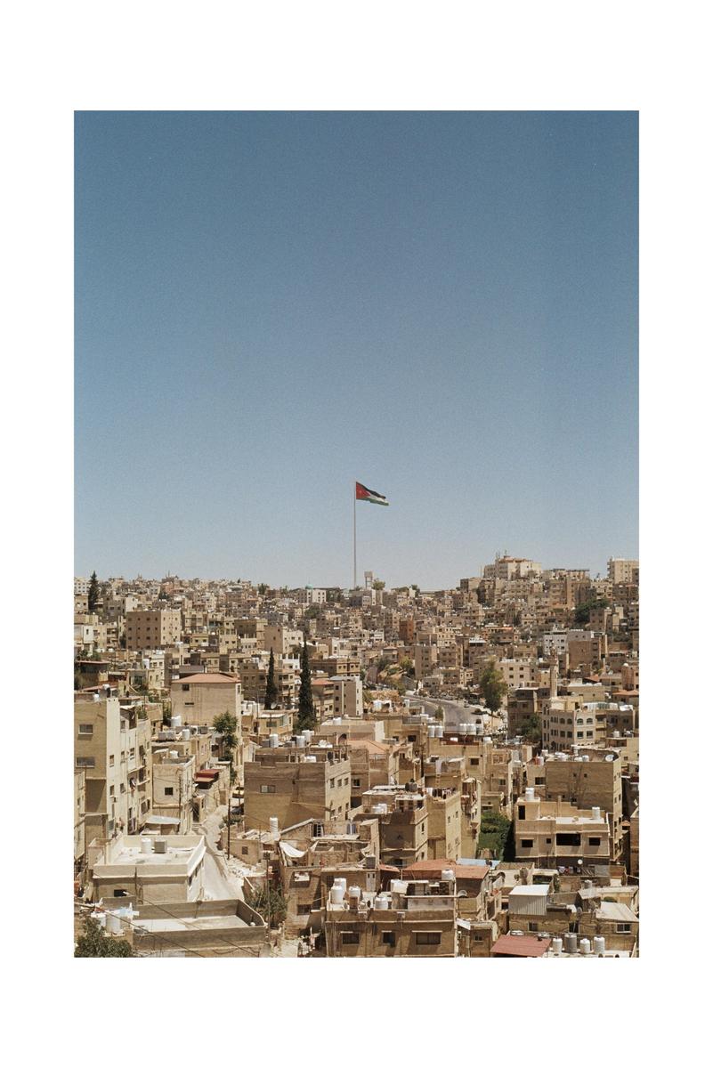 A flag flies above a city of buildings on a hill under a clear sky.