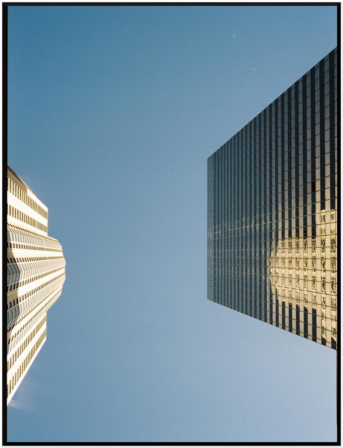 Two tall buildings are visible from a low angle against a clear blue sky.