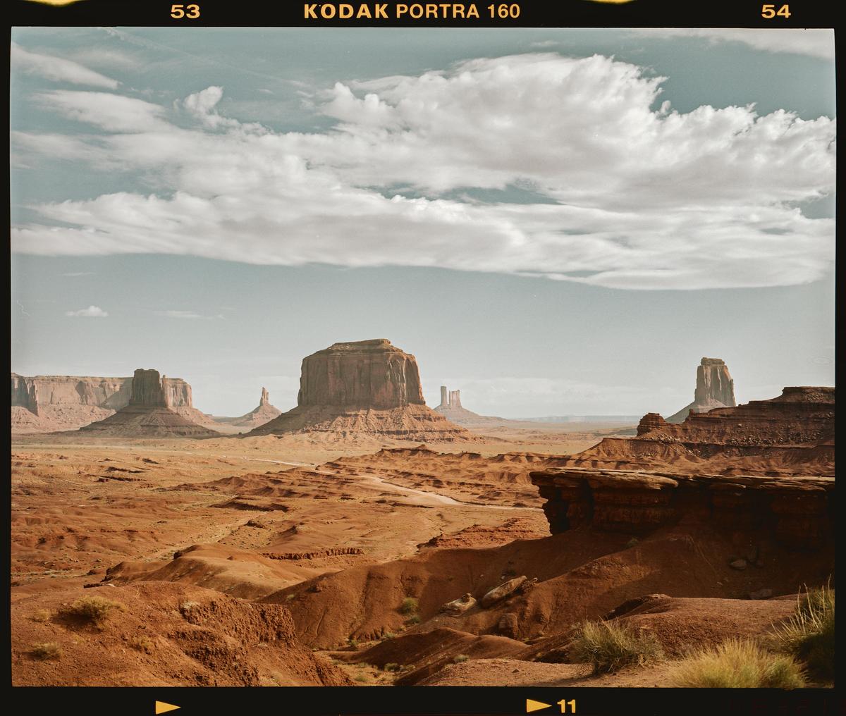A vast desert landscape features towering rock formations under a cloudy sky.