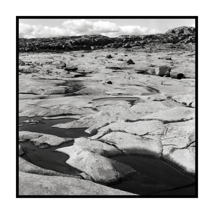 A rocky landscape with small pools of water and a cloudy sky.