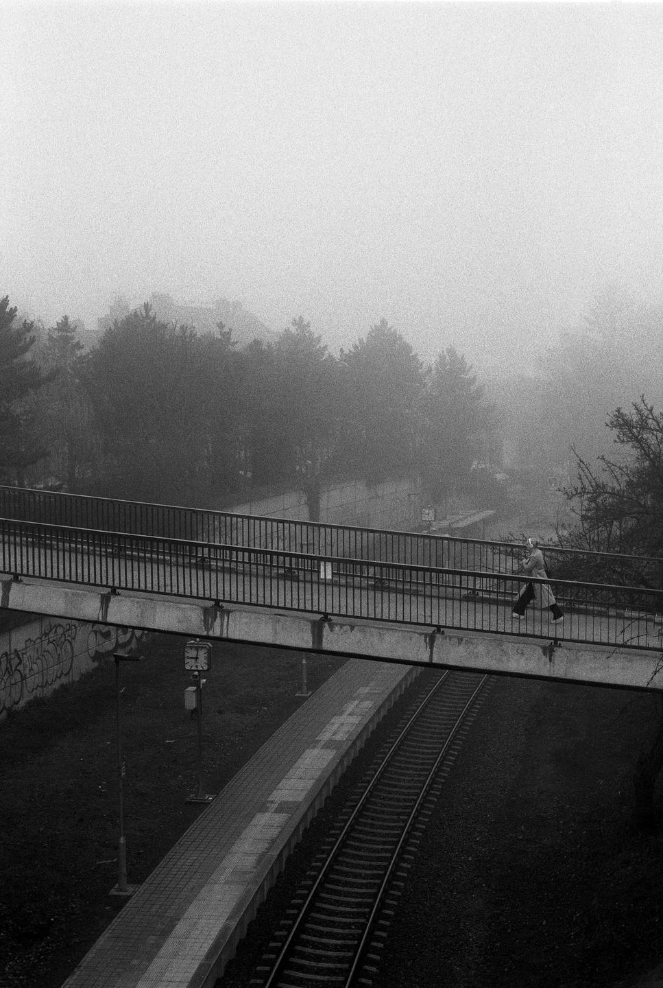 A person walks across a pedestrian bridge over train tracks on a foggy day.