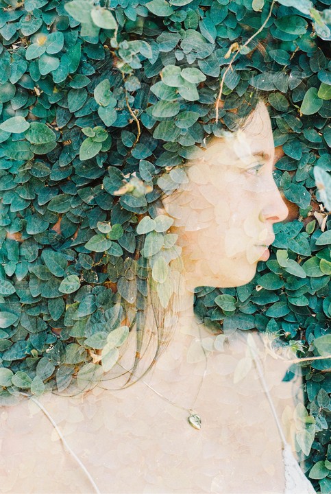 A woman's profile is visible through a double exposure with green leaves.