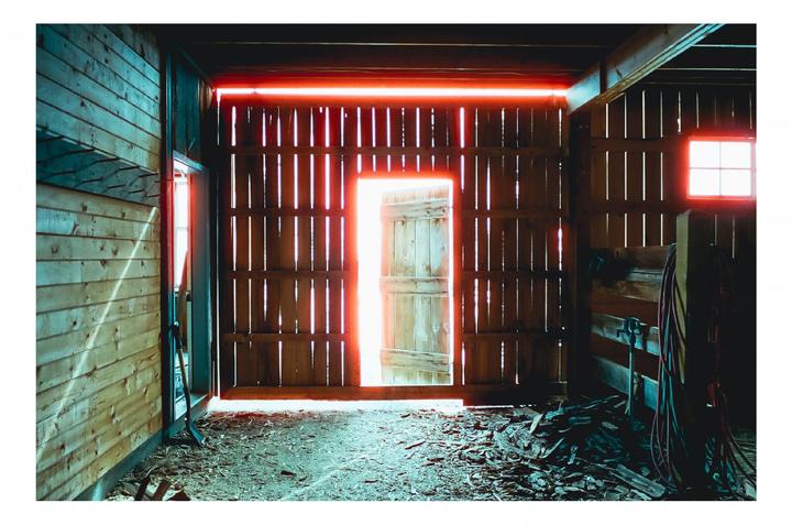 Sunlight streams through the open door and window of a wooden barn, illuminating dust motes in the air.