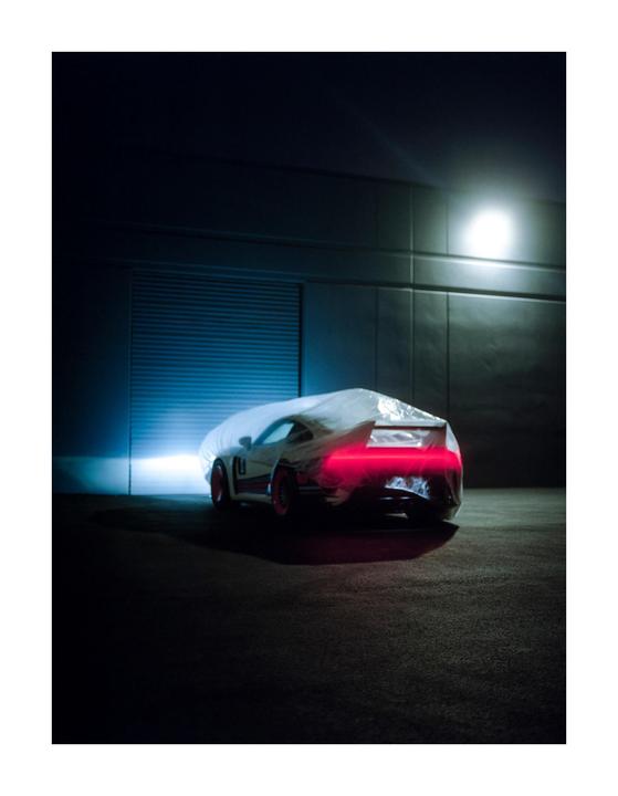 A car covered with a white sheet is parked in a dark garage with its red tail lights on.