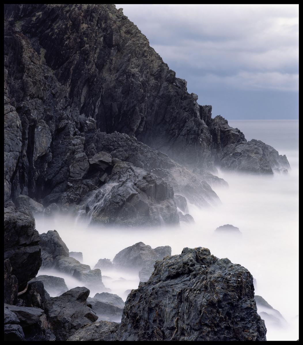 Waves crash against a rocky cliff, creating a misty effect over the water.