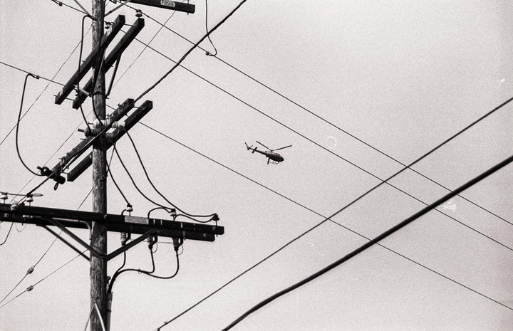 A helicopter flies in the sky behind a utility pole and power lines.
