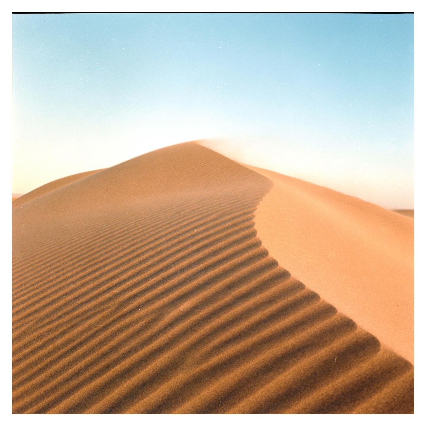 A large sand dune with ripples in the sand is visible under a clear sky.