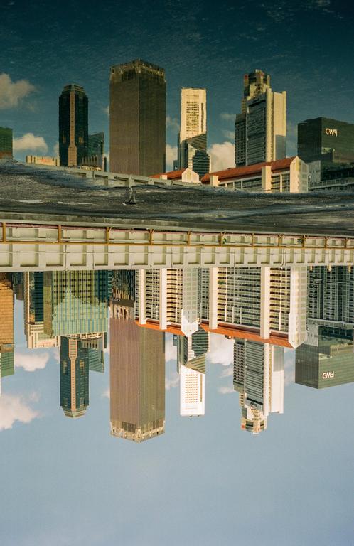 A cityscape with tall buildings is reflected in a body of water, creating an inverted image.