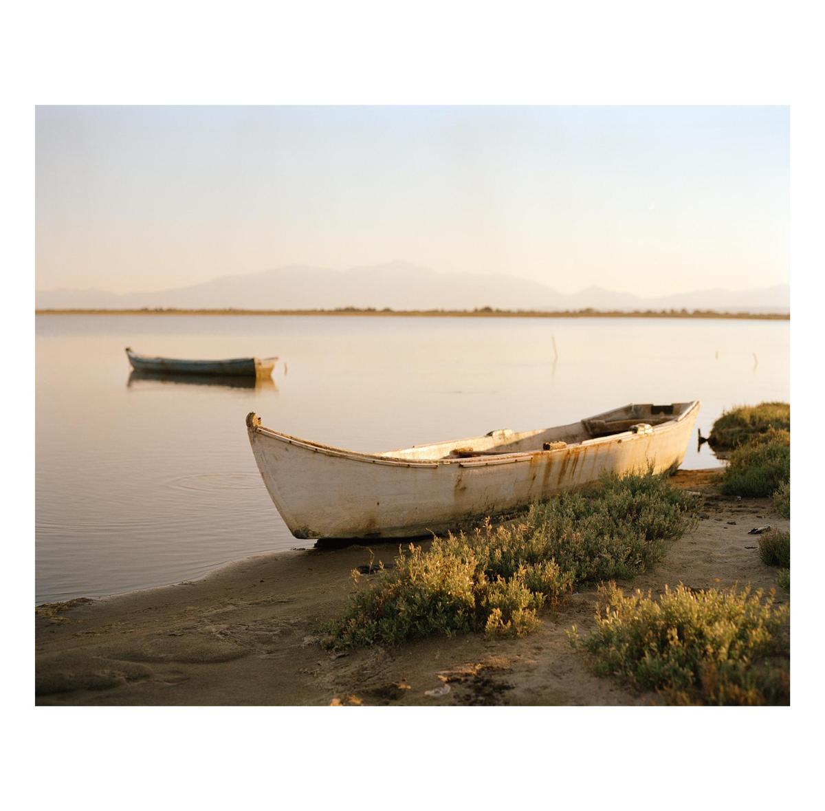 Two boats are on a body of water with mountains in the distance.