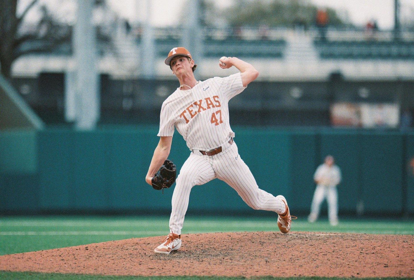 A baseball player in a white and orange uniform pitches from a mound on a baseball field.