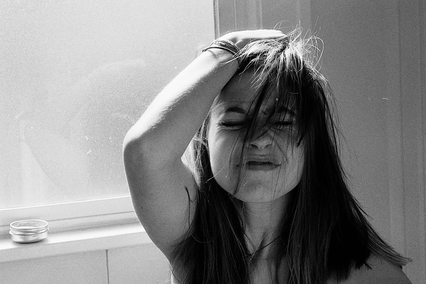 A woman with closed eyes and a pained expression holds her hand to her head, with her hair falling over her face.