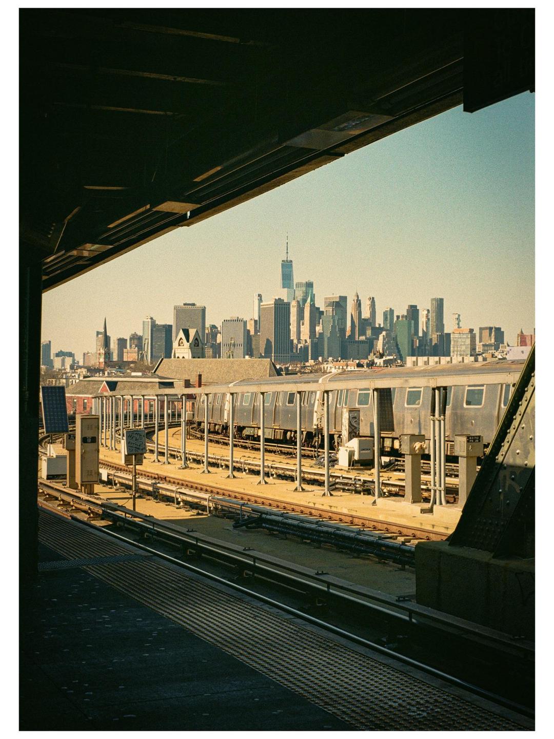 A subway platform overlooks train tracks with a city skyline in the distance.