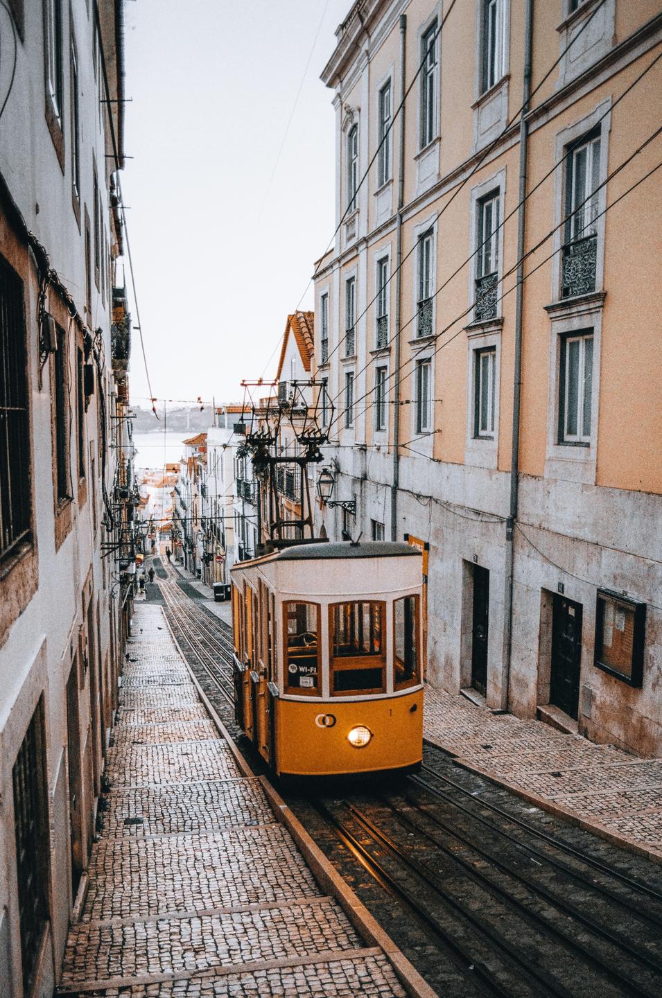A yellow tram travels down a narrow, cobblestone street lined with buildings in Lisbon.