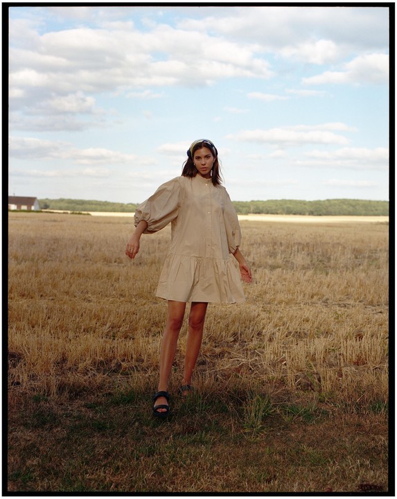 A woman stands in a field of cut crops under a cloudy sky.