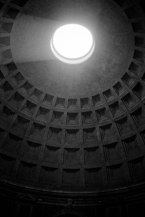 A beam of light shines through the oculus of the Pantheon, illuminating the coffered dome.
