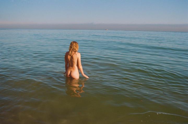 A woman stands in the ocean with her back to the viewer, looking out at the horizon.