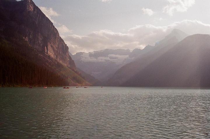 A wide shot shows a lake with several small boats and mountains in the background under a cloudy sky.
