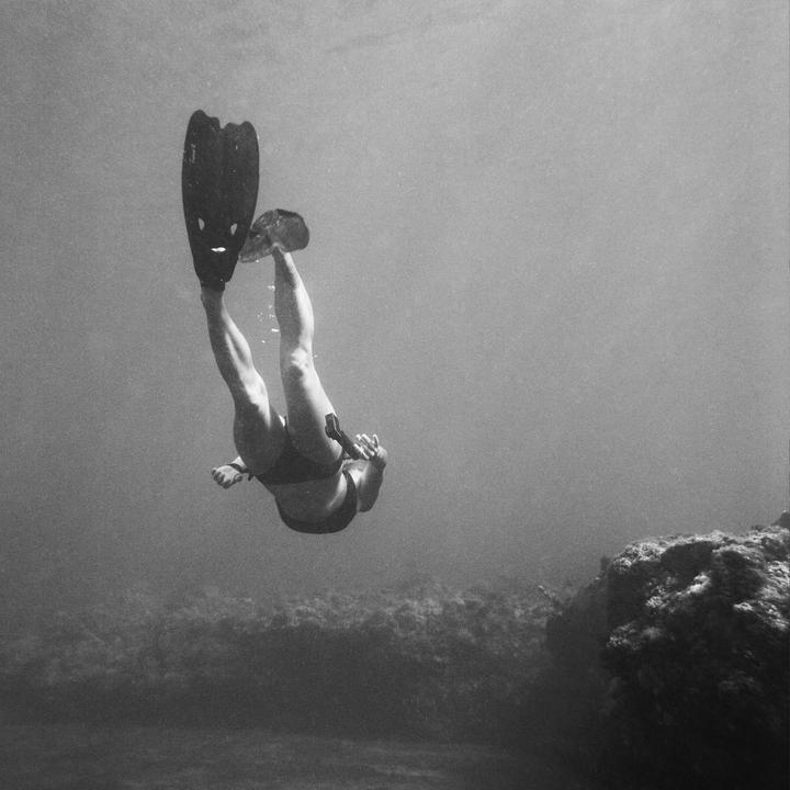 A person wearing flippers is swimming underwater near a rocky formation.