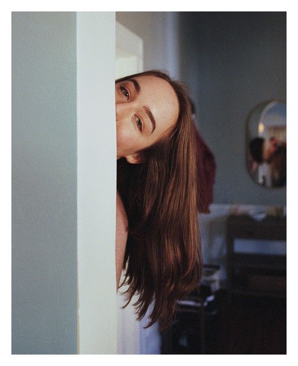 A woman peeks from behind a wall, with her hair flowing down.