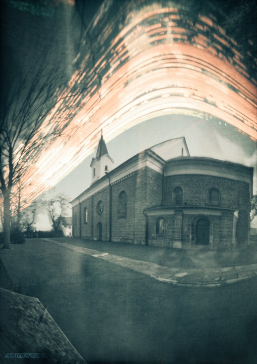 A church with a tall steeple stands under a sky with a bright, streaky light effect.