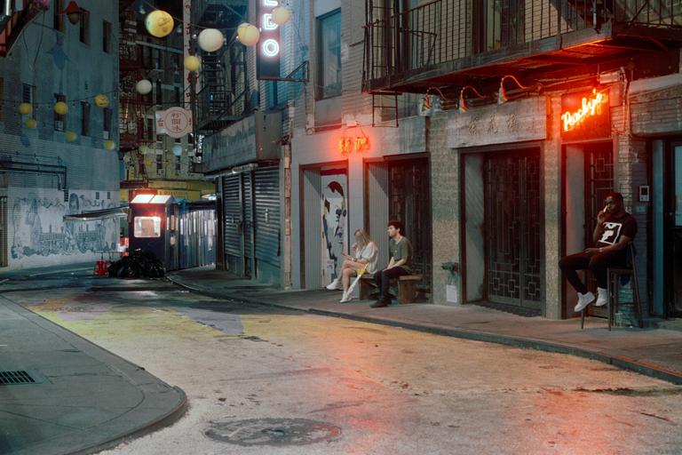 Three people are sitting on a street at night in Chinatown.