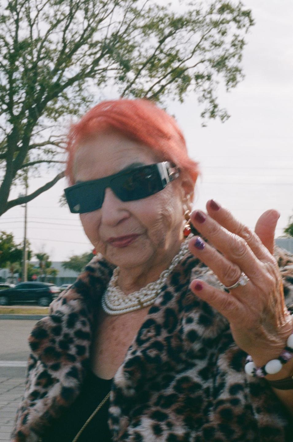 A woman with red hair, sunglasses, and a leopard print coat looks at the camera.