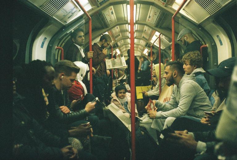 Many people are riding a subway train with red poles and arched ceilings.