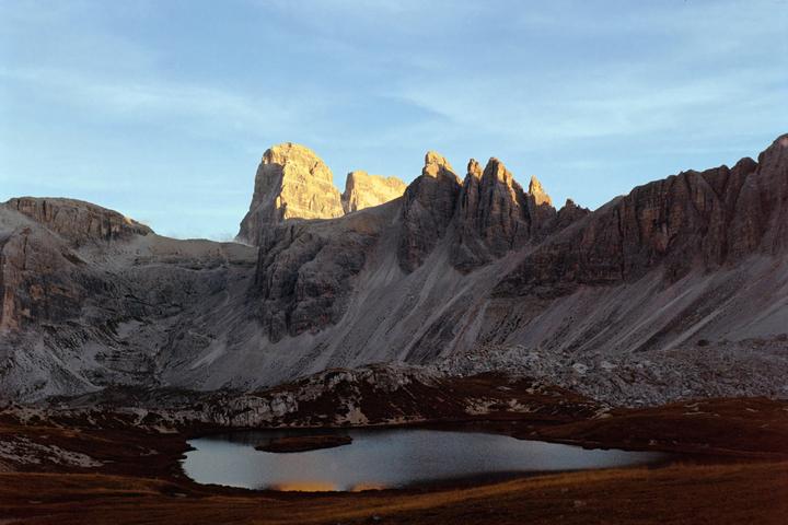 A small lake reflects the sky and mountains under a clear sky.