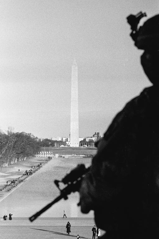 A person in silhouette holding a rifle looks out over the Washington Monument and the Reflecting Pool.