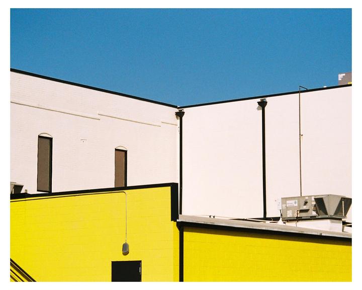 A bright yellow building is topped by a white building with two windows, all under a clear blue sky.