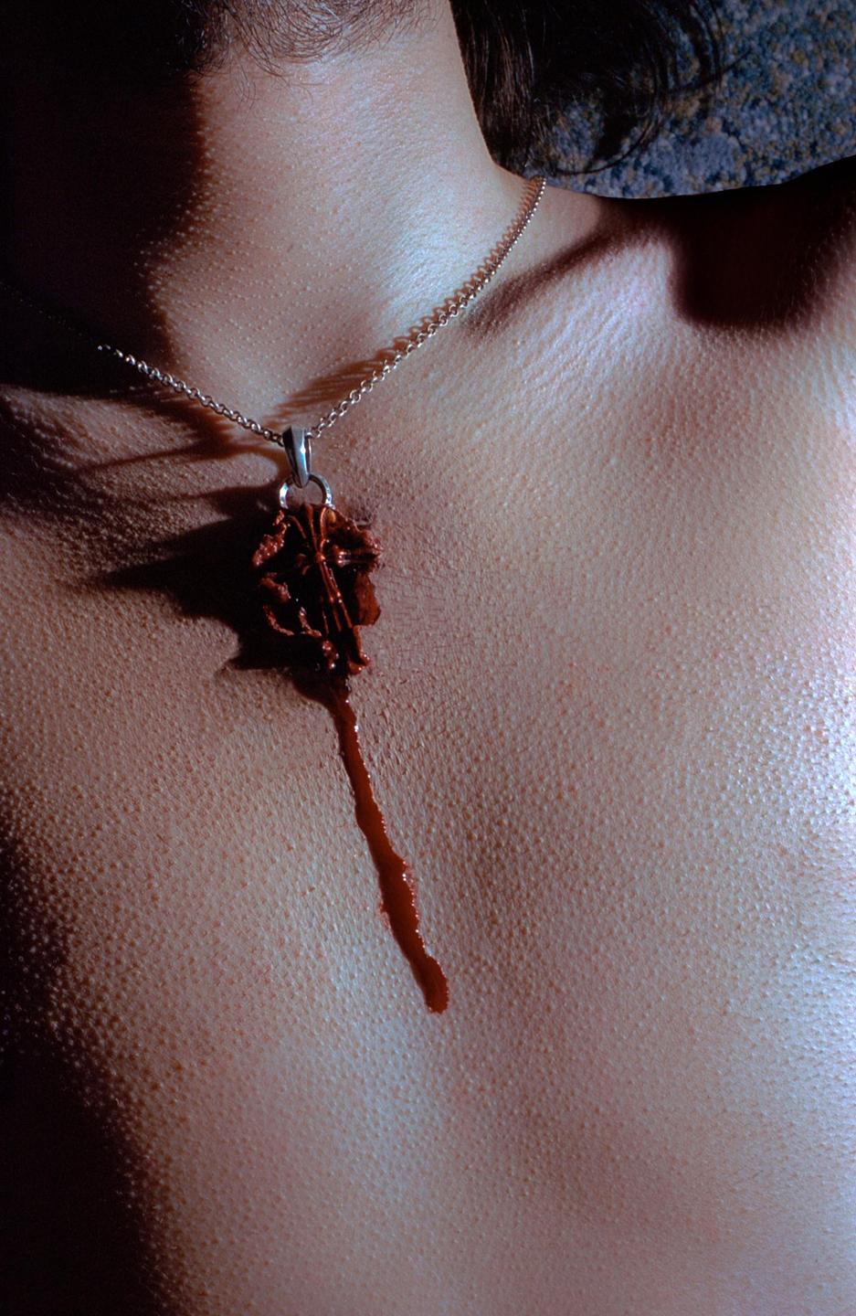 A necklace with a dark pendant hangs on a person's chest, with a dark liquid dripping from the pendant.