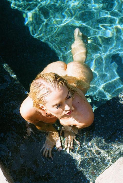 A woman with blonde hair is submerged in a swimming pool, looking up and to the right.