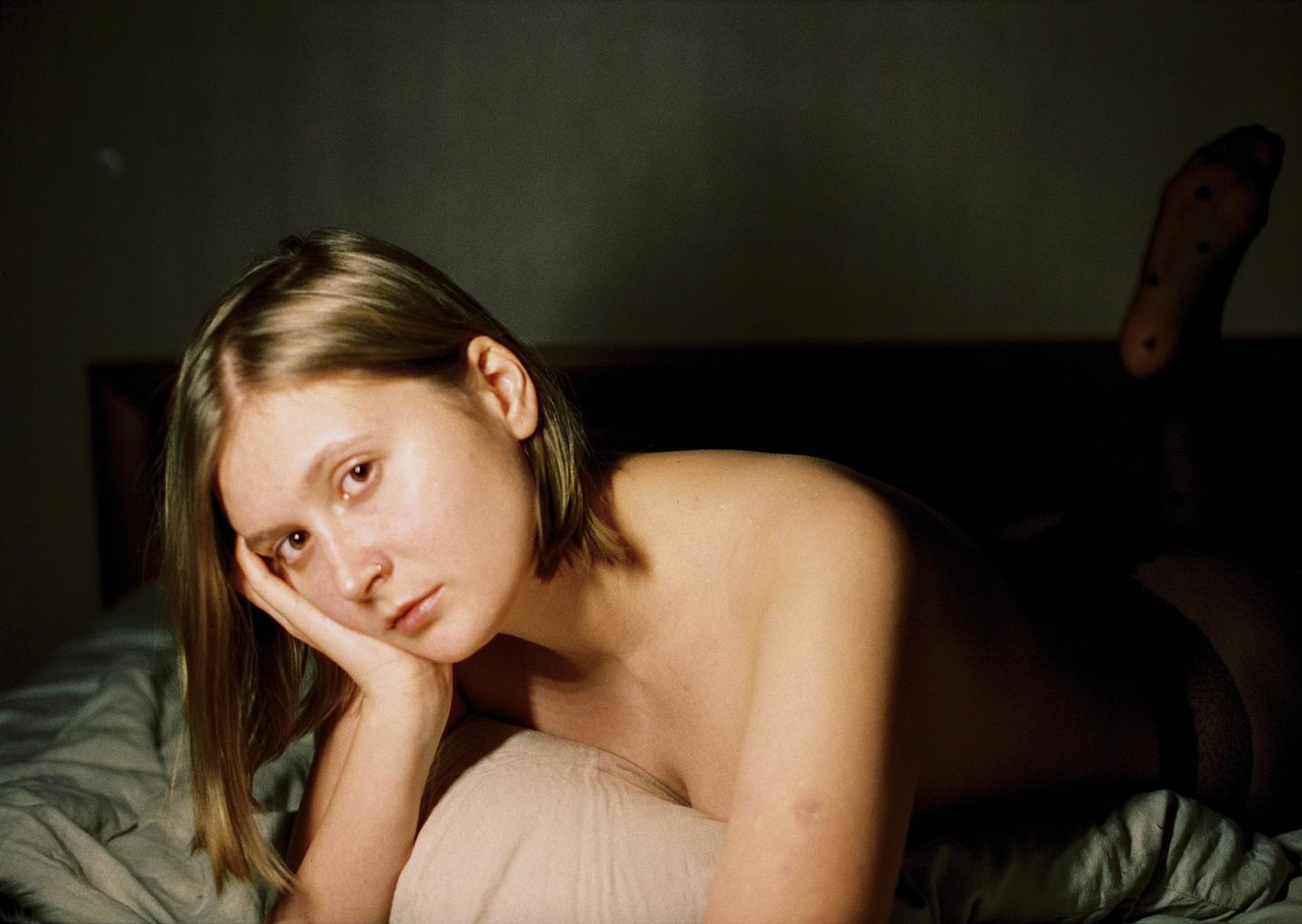 A woman with short hair lies on a bed, resting her head on her hand.