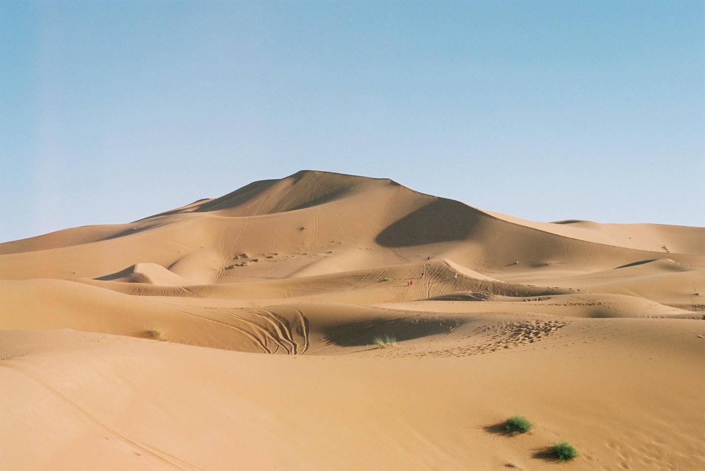 A vast desert landscape features rolling sand dunes under a clear sky.