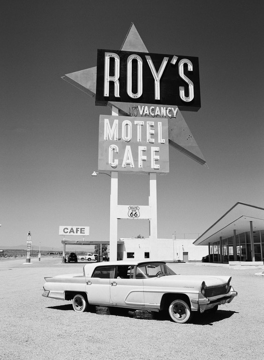 A vintage car is parked in front of Roy's Motel and Cafe sign on Route 66.