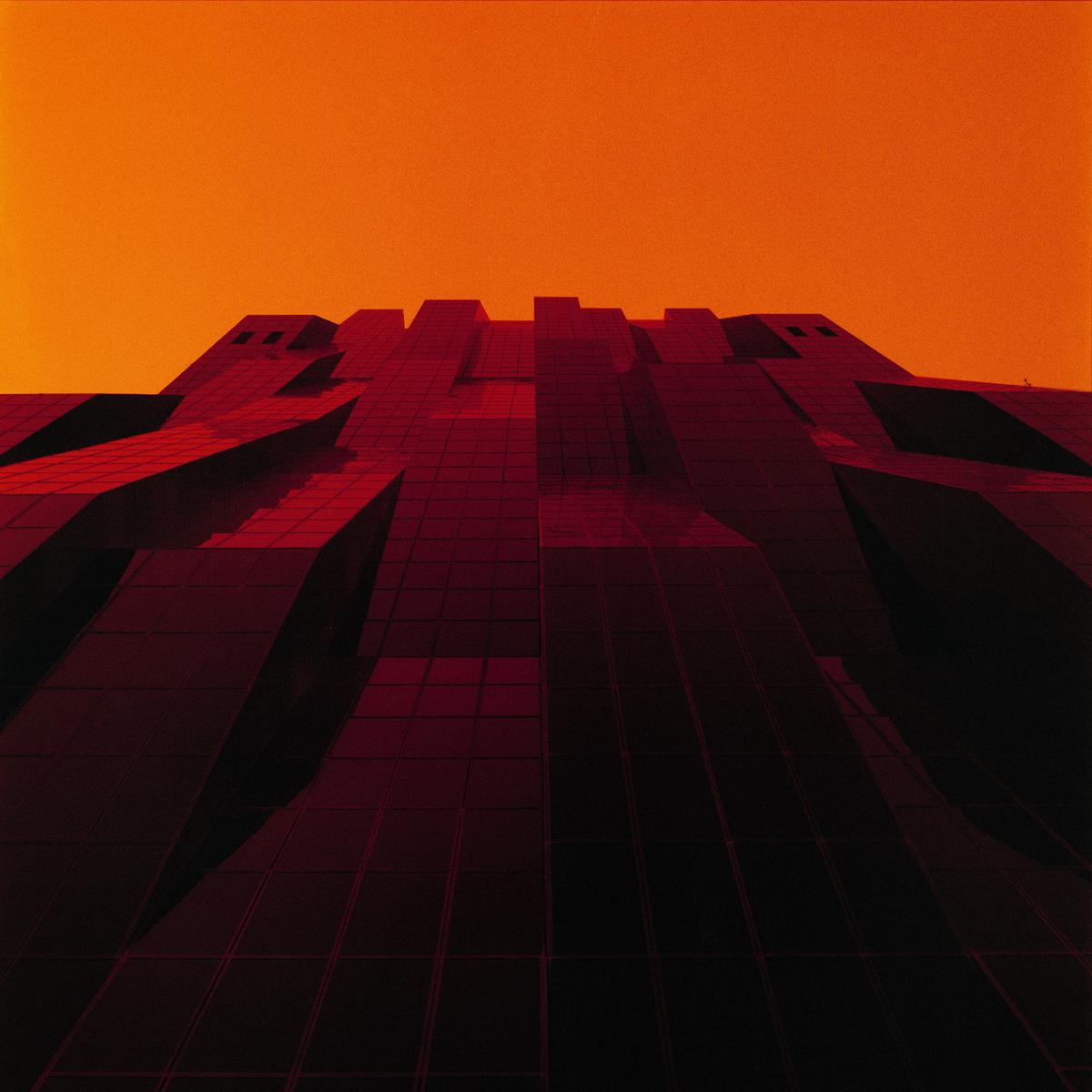 A large, dark, geometric building with many windows is visible against an orange sky.