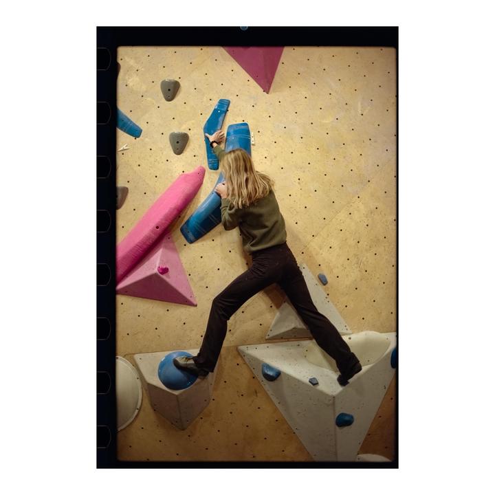 A woman climbs an indoor rock wall with colorful holds.