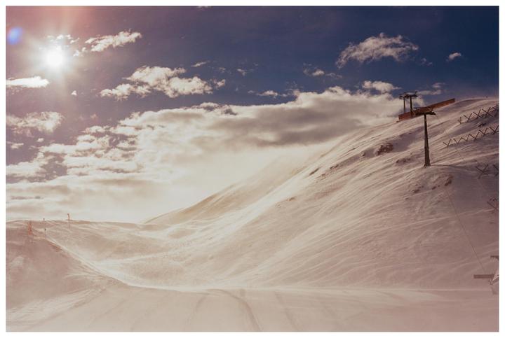 A snow-covered mountain with a ski lift under a bright sun and cloudy sky.