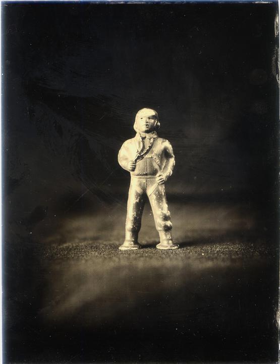 A small, worn figurine of a person in a jumpsuit stands against a dark background.