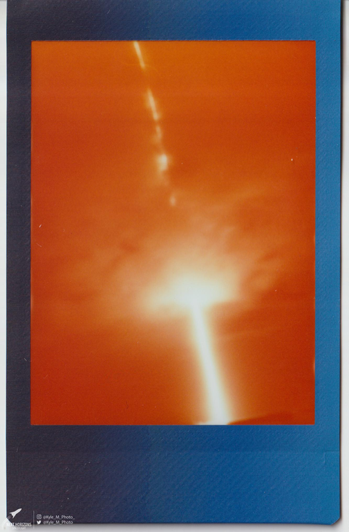 A bright light shoots upwards from a glowing cloud against an orange sky.
