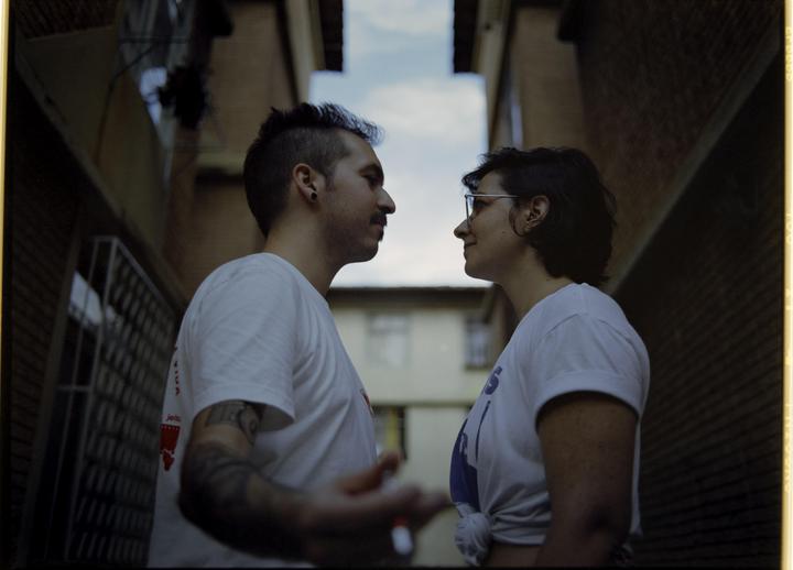 A couple stands facing each other in an alleyway between two buildings.