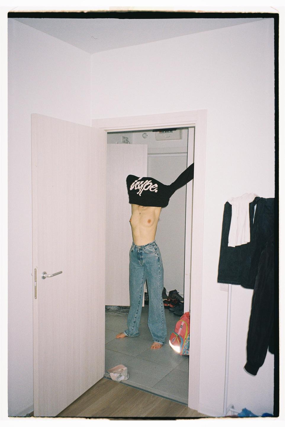A woman stands in a doorway, pulling a black sweatshirt over her head.