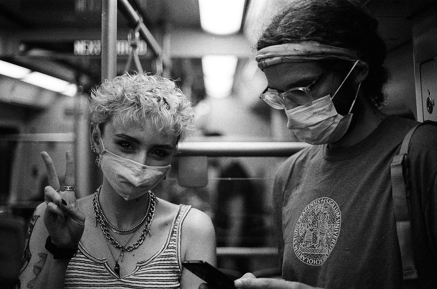 A woman and a man wearing masks are riding a subway.
