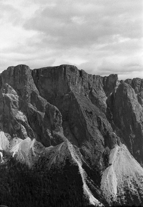 A dramatic black and white landscape shows a rugged mountain range under a cloudy sky.