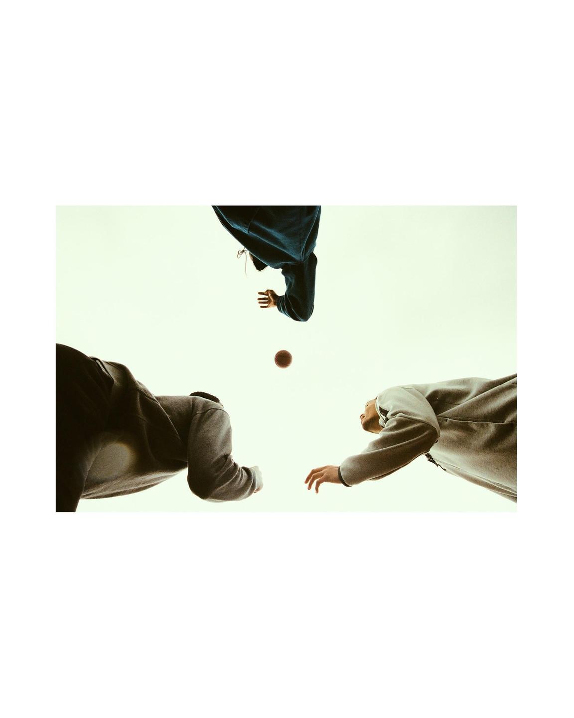Three people in hoodies reach for a basketball against a light background.