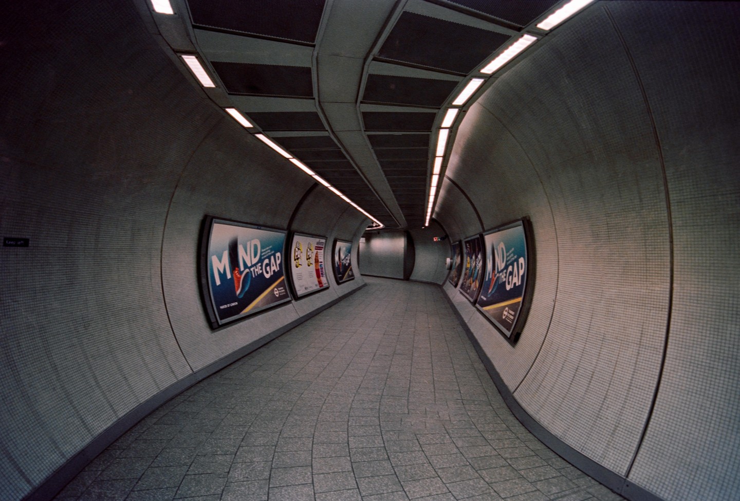 A long, curved underground tunnel is illuminated by overhead lights and lined with advertisements.