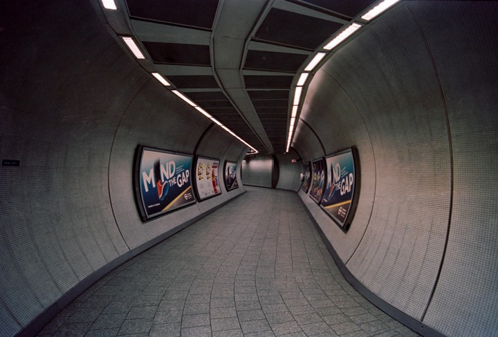 A long, curved underground tunnel is illuminated by overhead lights and lined with advertisements.